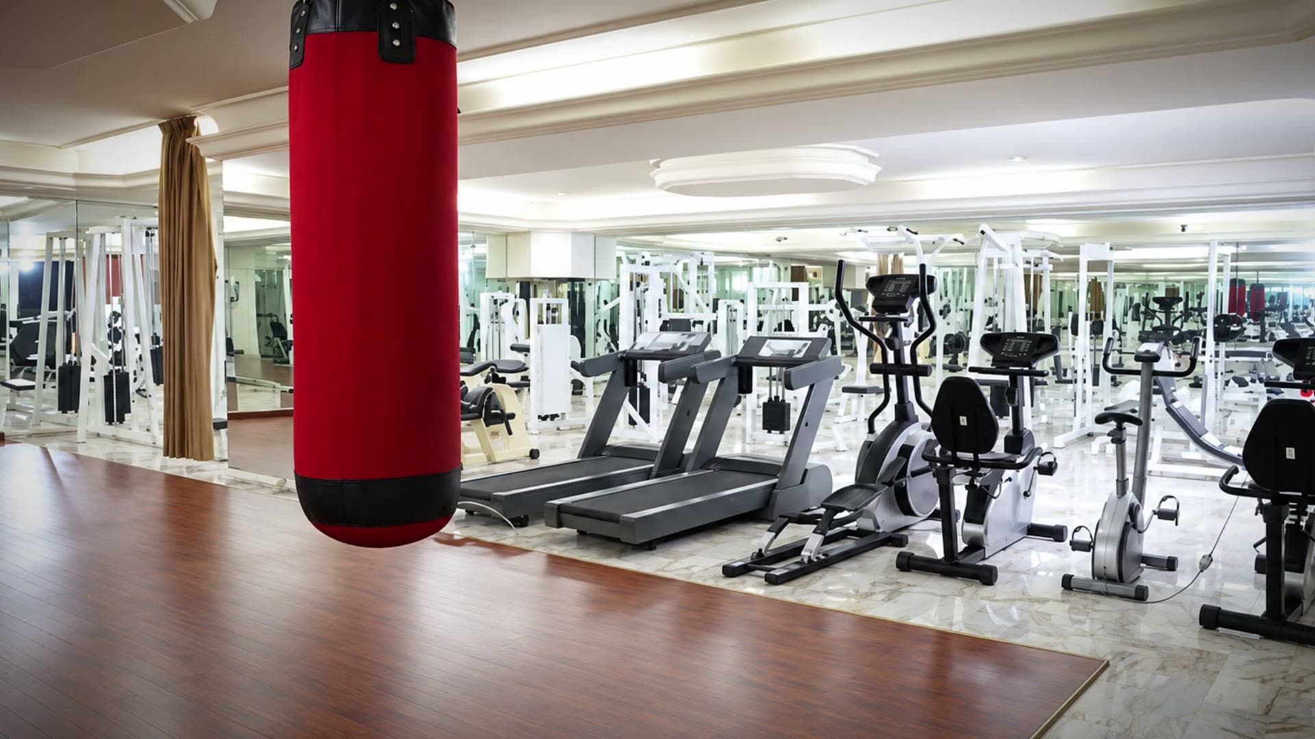 La salle de Viccini Club : tapis de course, vélos et un sac de frappe rouge dans une salle lumineuse aux murs de miroirs